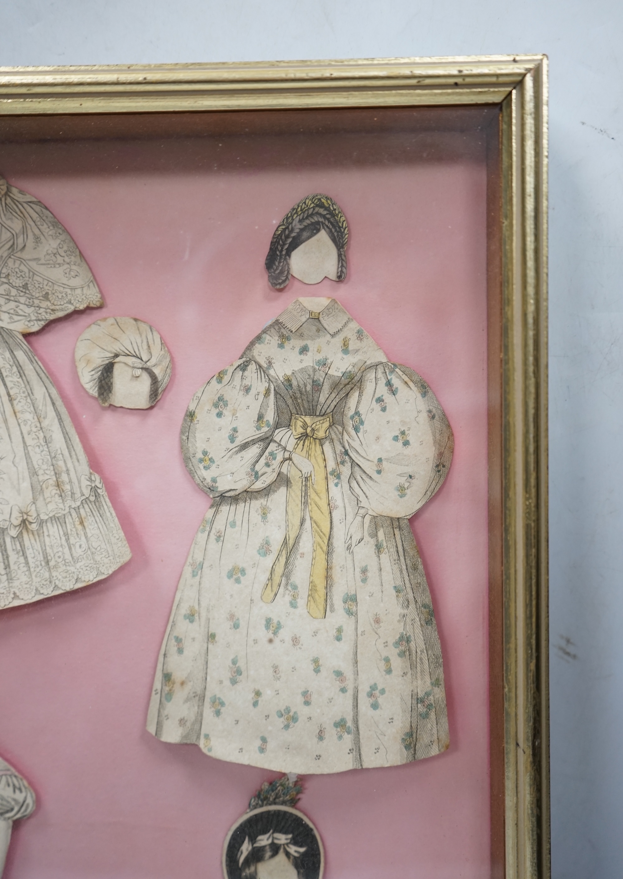 An early 19th century framed Rudolph Ackermann La Poupee-Modele paper doll set, comprising of a double sided doll in lingerie with wooden stand, five double sided gowns and five bonnets, dimensions of the frame; 40cm wid